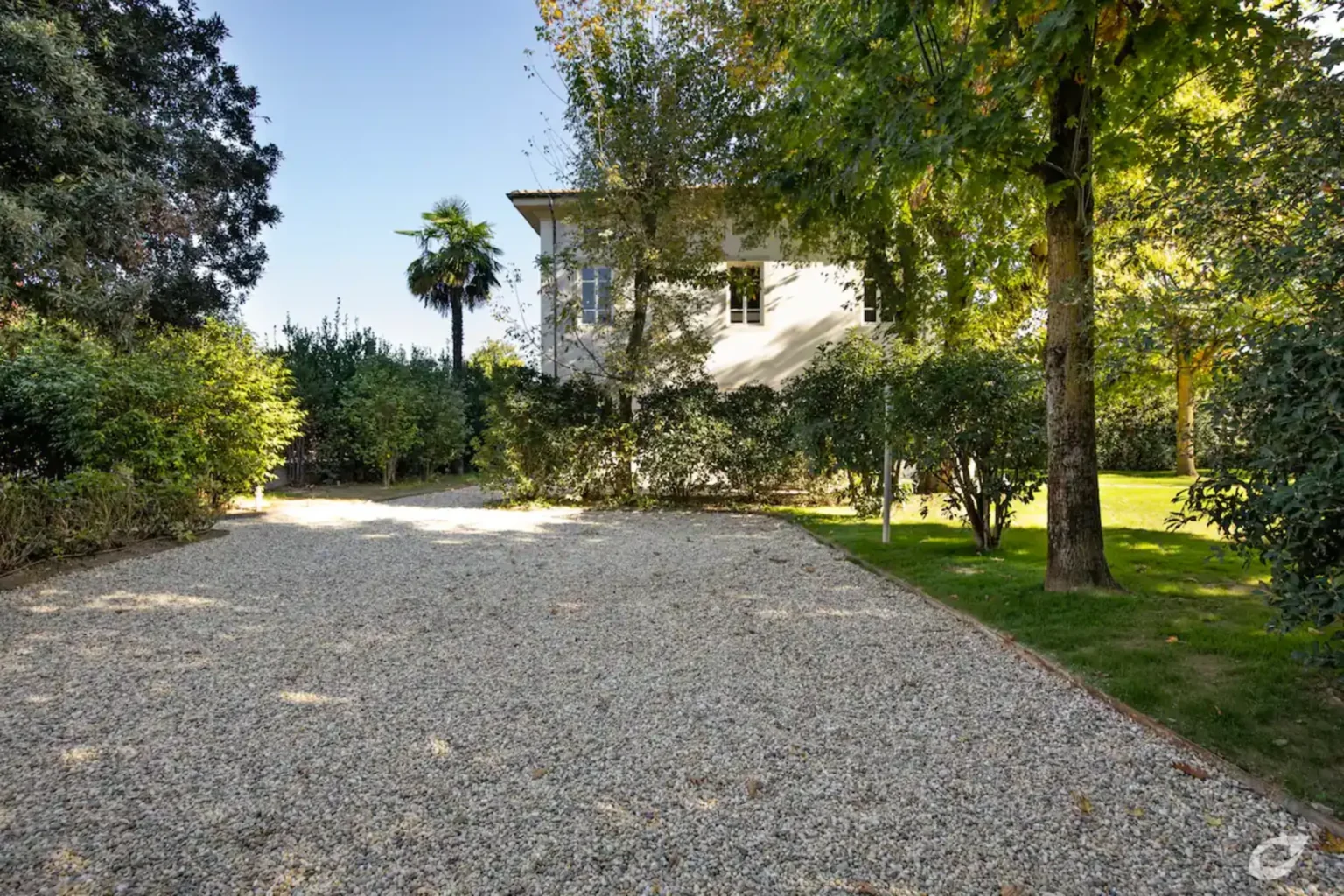 Gravel driveway leading to a charming house surrounded by lush greenery and trees, creating a serene outdoor environment. | Only on SopranoVillas