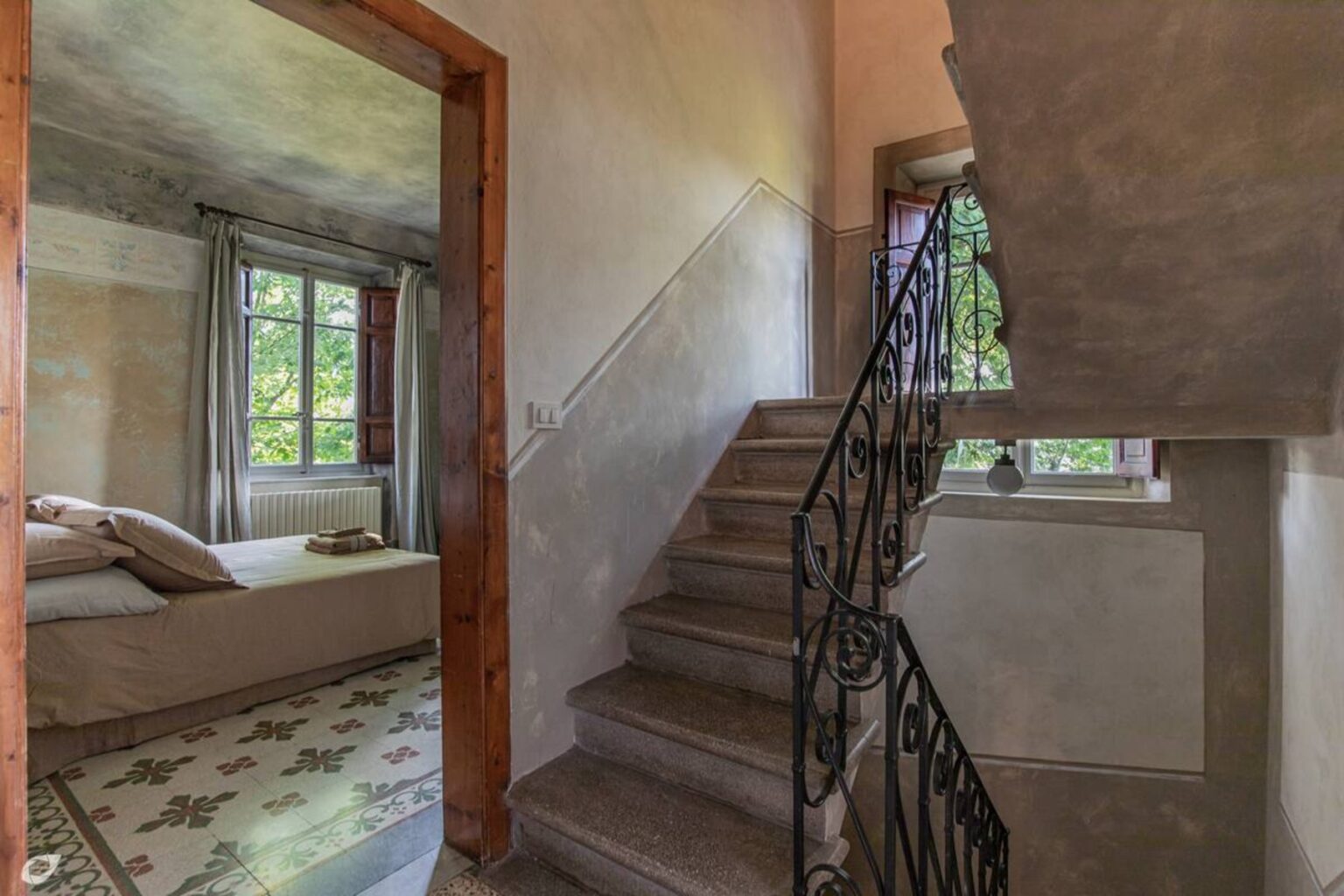 Interior view of a stylish home featuring a staircase with decorative iron railing, leading to an upper level, and a glimpse of a cozy bedroom with large windows and natural light. | Only on SopranoVillas