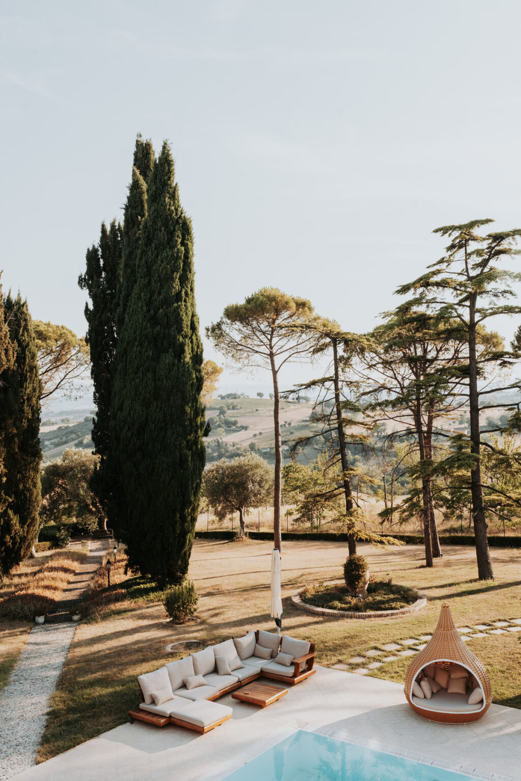 Scenic view of rolling hills in the countryside, framed by tall cypress and pine trees under a clear sky. | Only on SopranoVillas