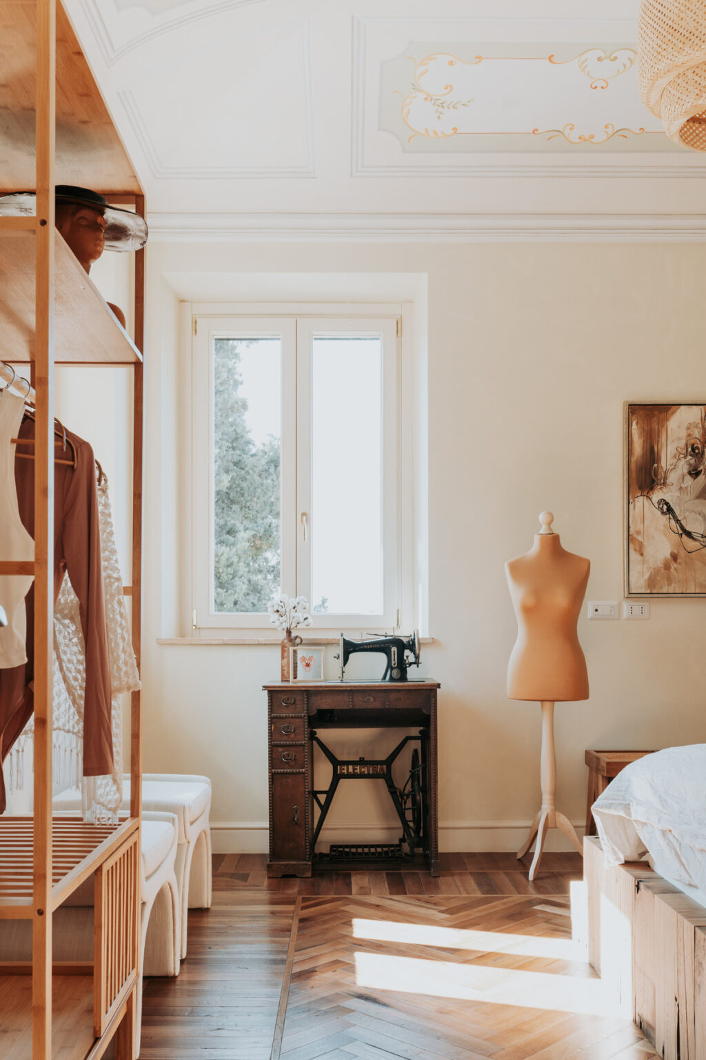 Cozy sewing room featuring a dressmaker's mannequin, vintage sewing machine, and natural light streaming through a large window, with organized clothing on a wooden rack and artistic decor on the walls. | Only on SopranoVillas