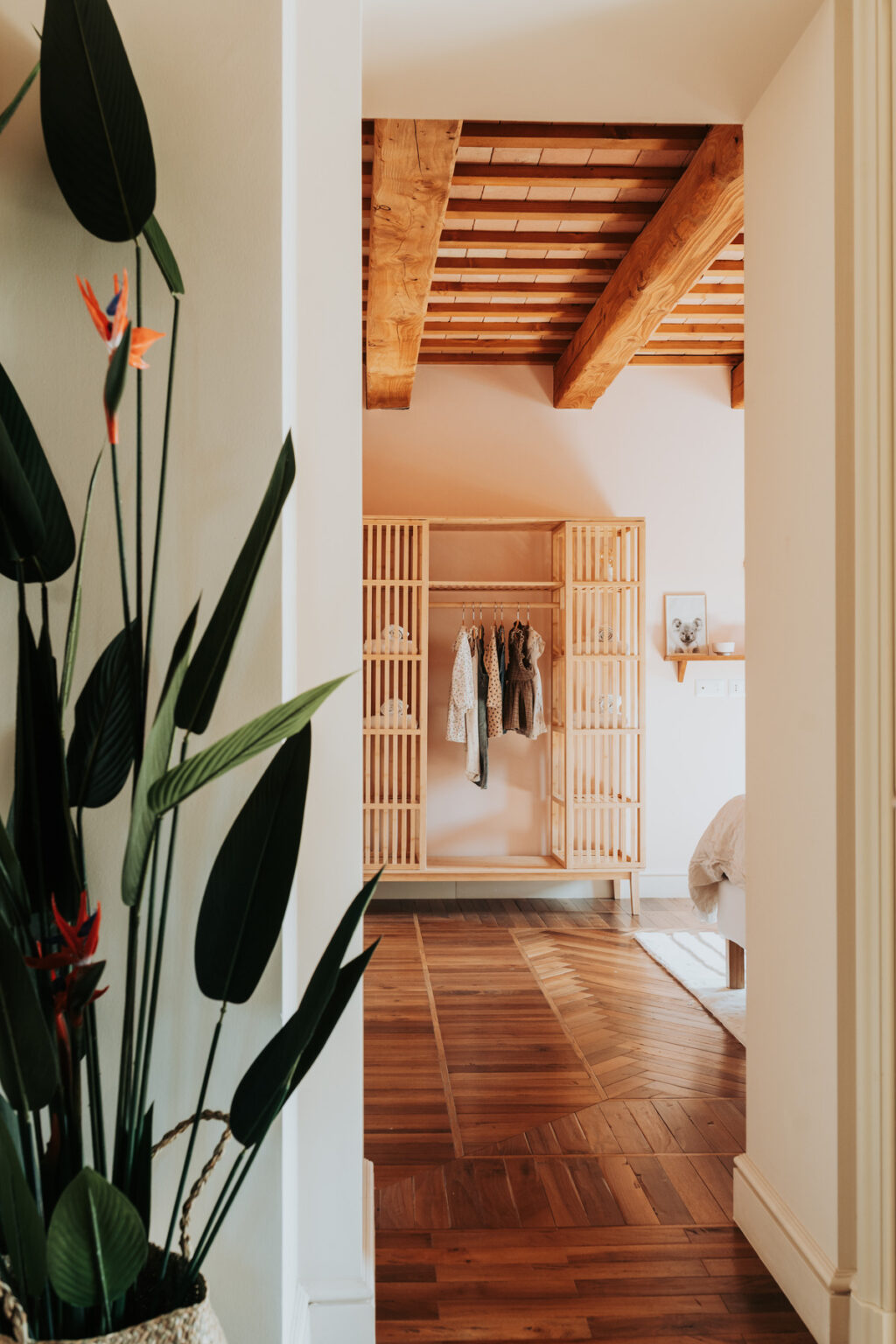 Interior view of a stylish bedroom featuring a wooden wardrobe with open shelving, neatly displaying clothing. Lush green plants are visible in the foreground, enhancing the room's natural aesthetic and inviting atmosphere. | Only on SopranoVillas