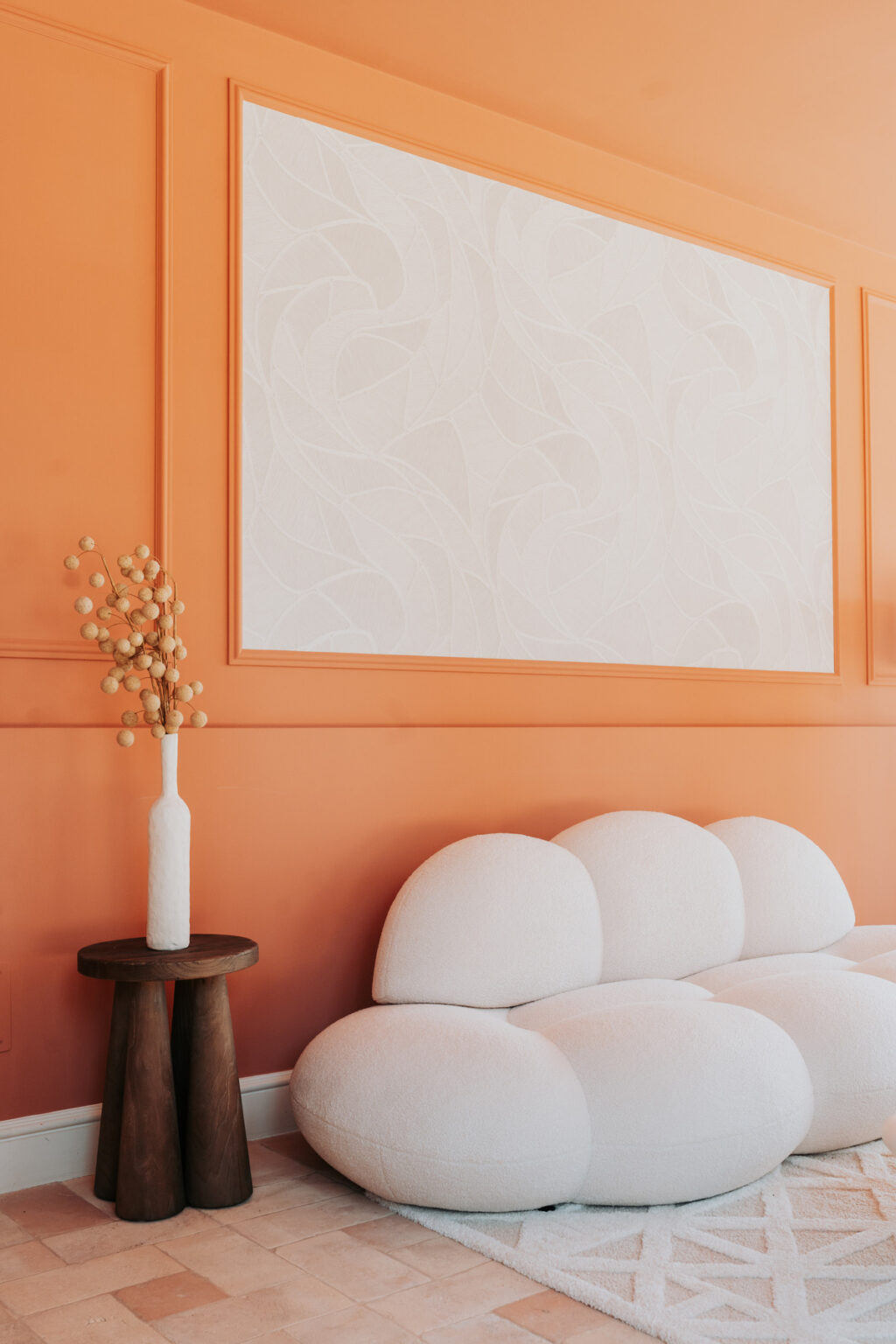 Modern interior design featuring an orange wall with subtle floral patterns, a white vase with decorative branches, and a minimalist white sofa, creating a stylish and inviting living space. | Only on SopranoVillas