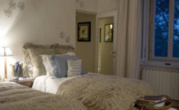 Cozy bedroom with two twin beds, decorated with floral bedding and plush pillows, featuring soft lighting and a window with evening views, creating a warm and inviting atmosphere.