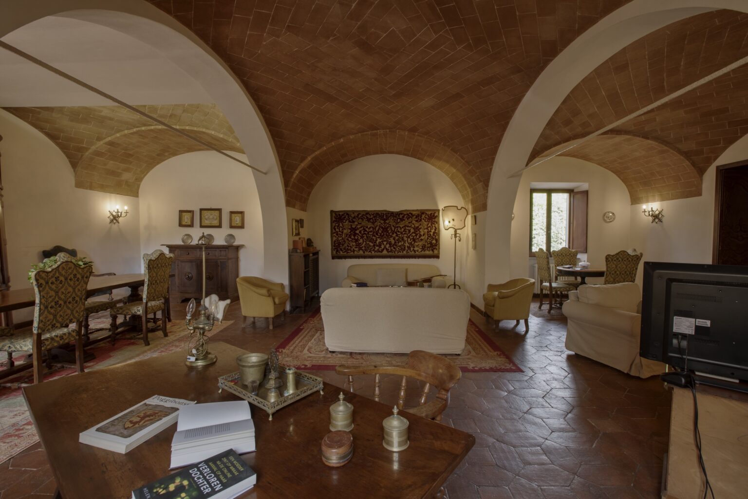 Spacious living room with arched ceilings, elegant furniture, and warm lighting, featuring a cozy seating area, wooden dining table, and decorative accents, ideal for relaxation and entertaining. | Only on SopranoVillas