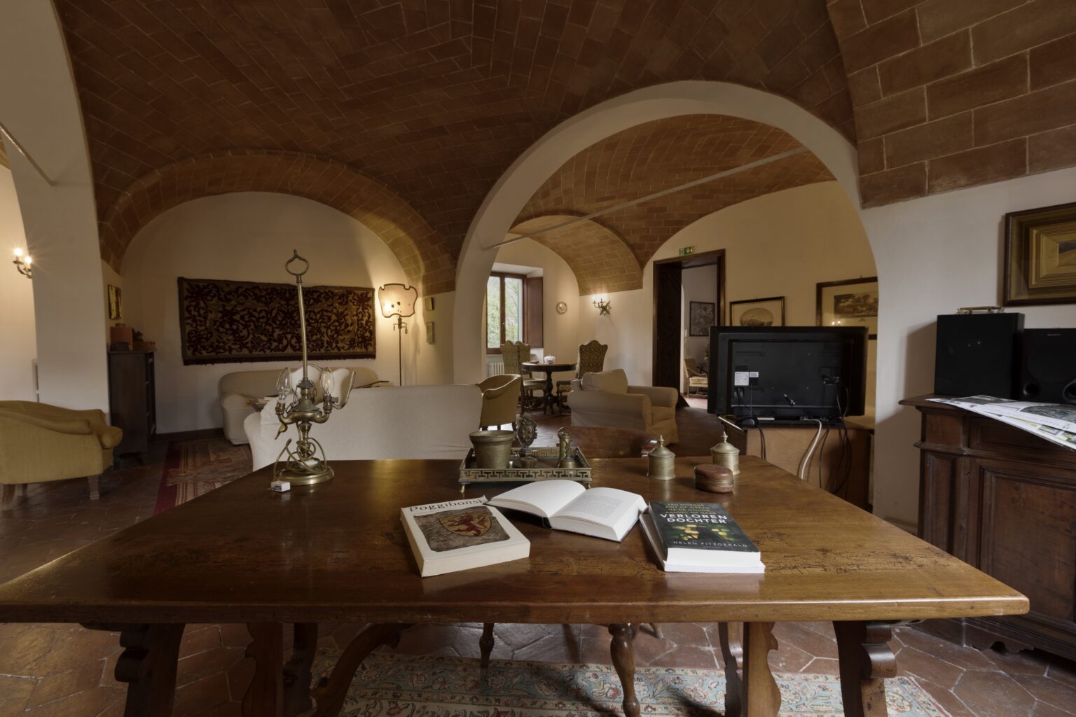 Cozy living room interior featuring a wooden dining table with books, arched ceilings, and warm lighting, creating an inviting atmosphere. | Only on SopranoVillas