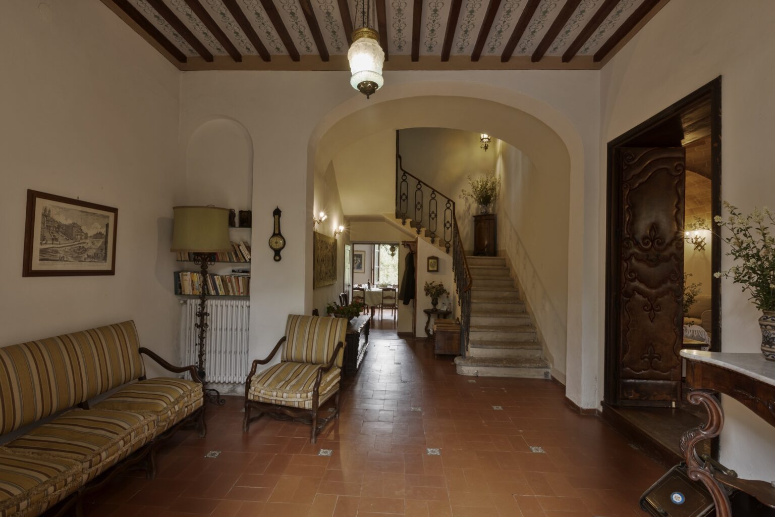 Spacious entryway with wooden beams, featuring a cozy seating area and a staircase leading to the upper floor, adorned with decorative art and warm lighting. | Only on SopranoVillas