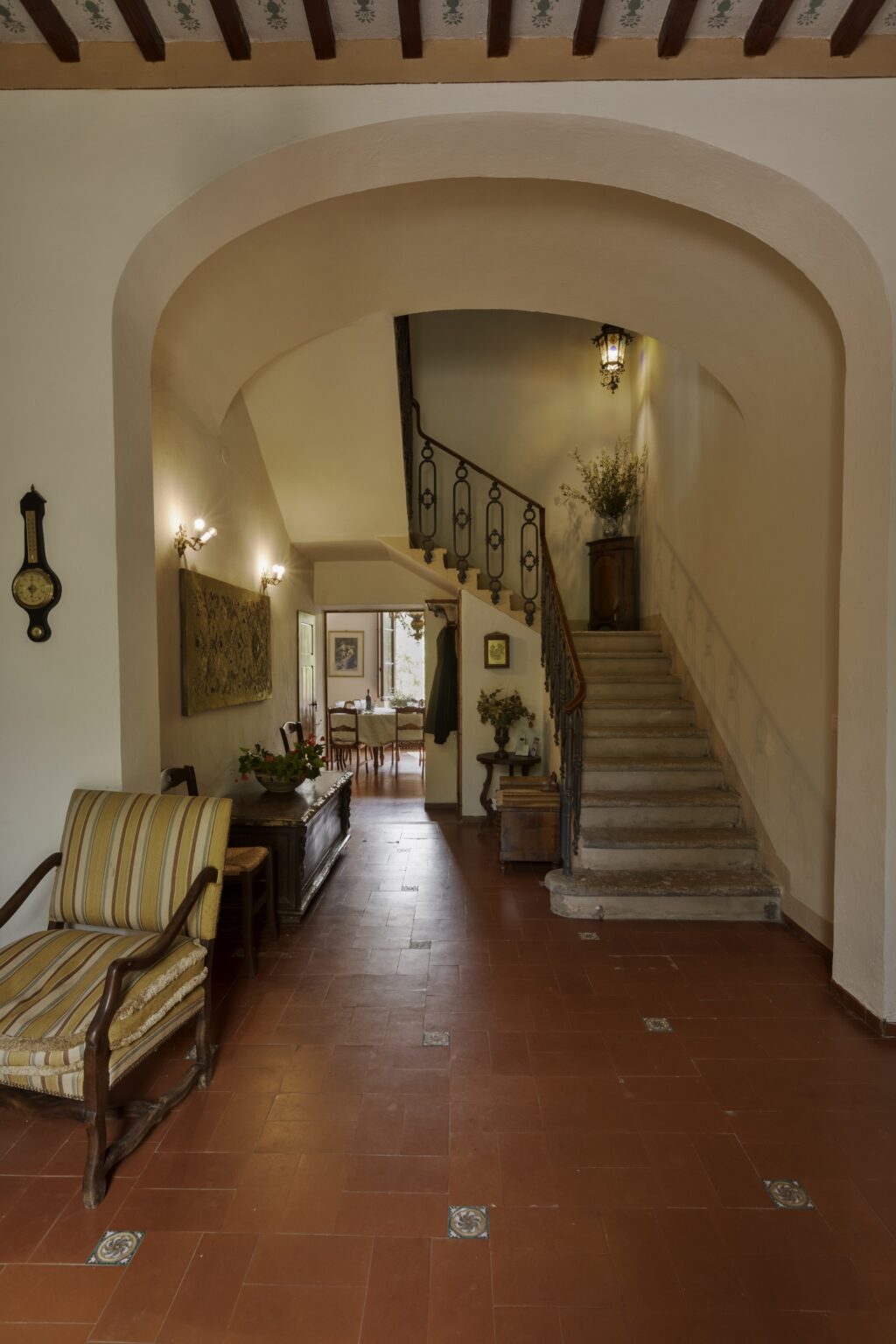 Interior view of a welcoming hallway featuring a staircase, vintage decor, and a cozy seating area. The space is well-lit, showcasing a blend of classic and modern design elements, with plants and artwork enhancing the ambiance. | Only on SopranoVillas