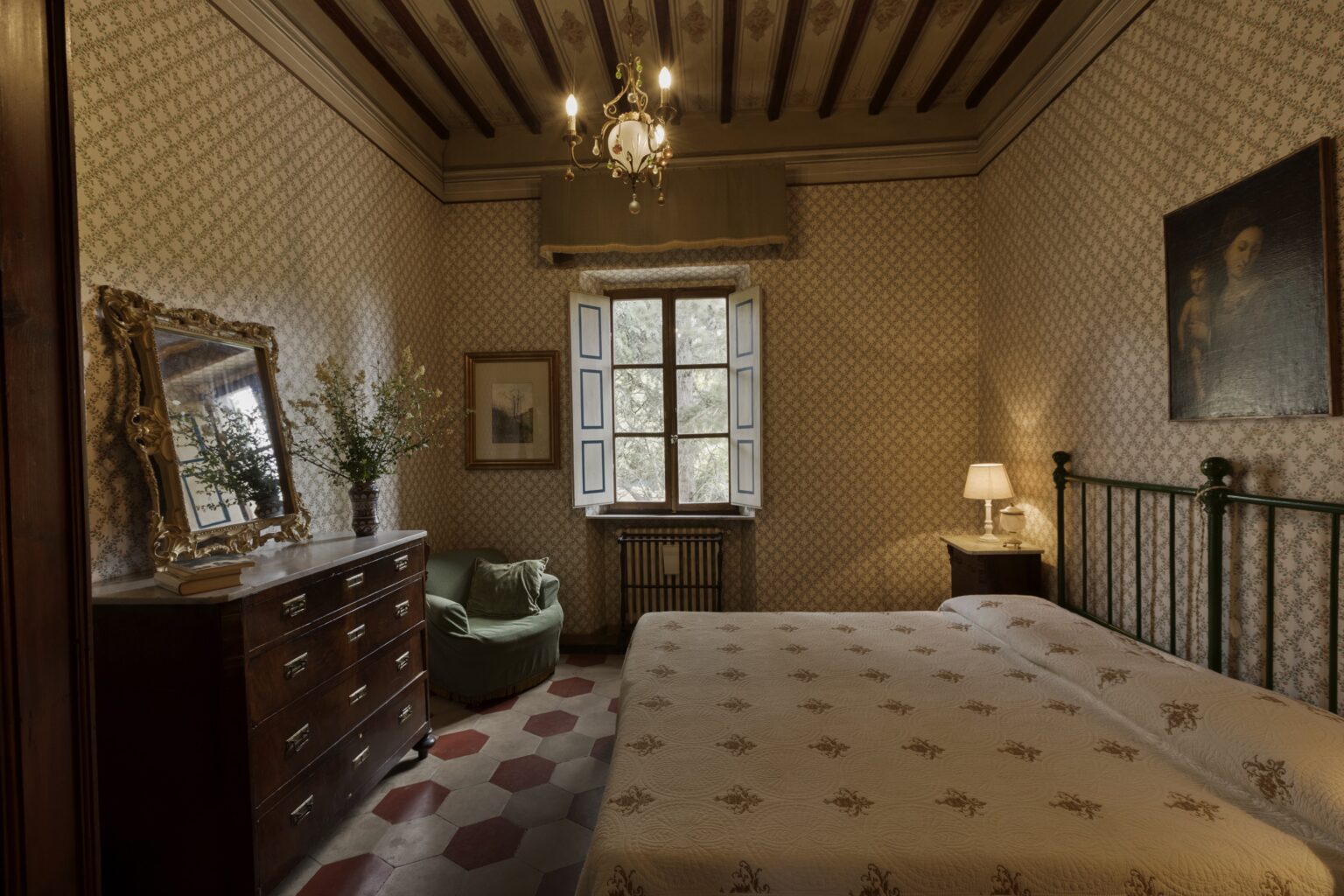 Cozy bedroom featuring a double bed, vintage wooden furniture, a decorative mirror, and a stylish chandelier, with natural light streaming through a window and a green armchair in the corner. | Only on SopranoVillas