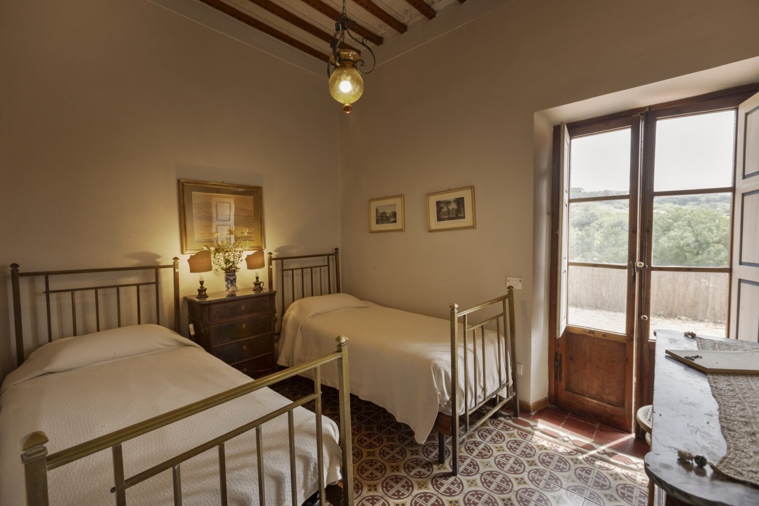 Cozy bedroom featuring two twin beds with metal frames, wooden accents, and a window that opens to a scenic view. The room is softly lit with warm tones, showcasing charming decor and a welcoming atmosphere. Ideal for a comfortable stay. | Only on SopranoVillas