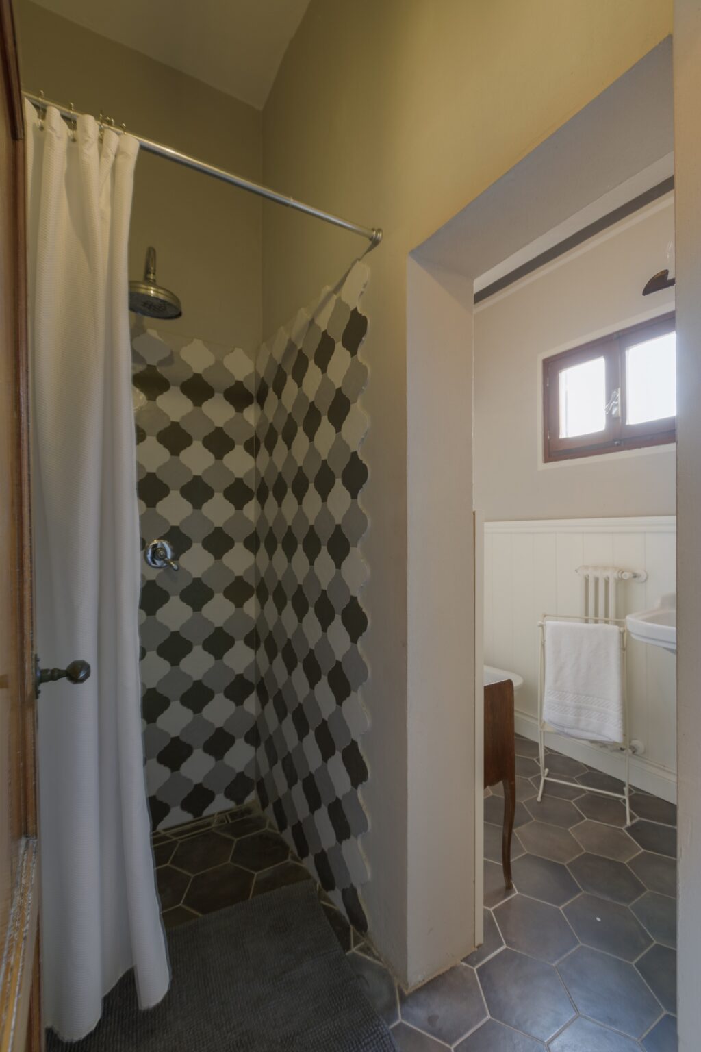 Modern bathroom featuring a stylish shower with a geometric patterned curtain, natural light from a window, and a clean, organized space with white towels and a minimalistic design. | Only on SopranoVillas