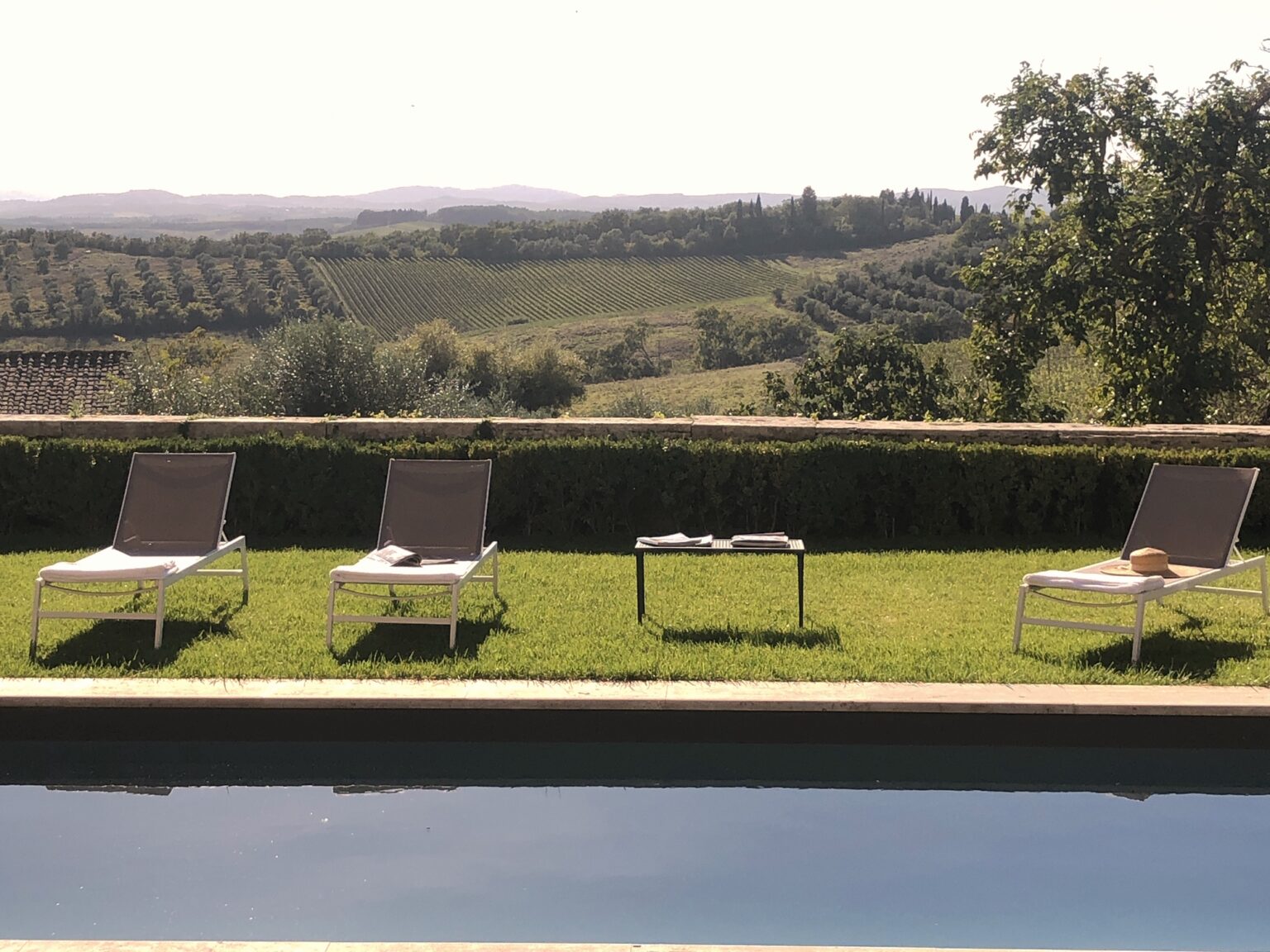 Relaxing outdoor setting with three lounge chairs beside a swimming pool, overlooking lush vineyards and rolling hills in the background. Ideal for a tranquil getaway or vacation retreat. | Only on SopranoVillas