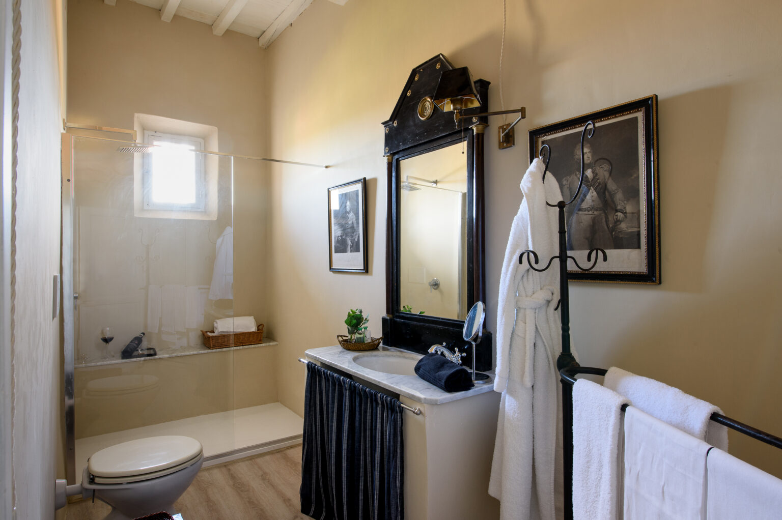 Modern bathroom design featuring a glass shower, stylish black and white decor, a vintage mirror, and neatly arranged towels. Natural light illuminates the space, enhancing its elegant ambiance. | Only on SopranoVillas