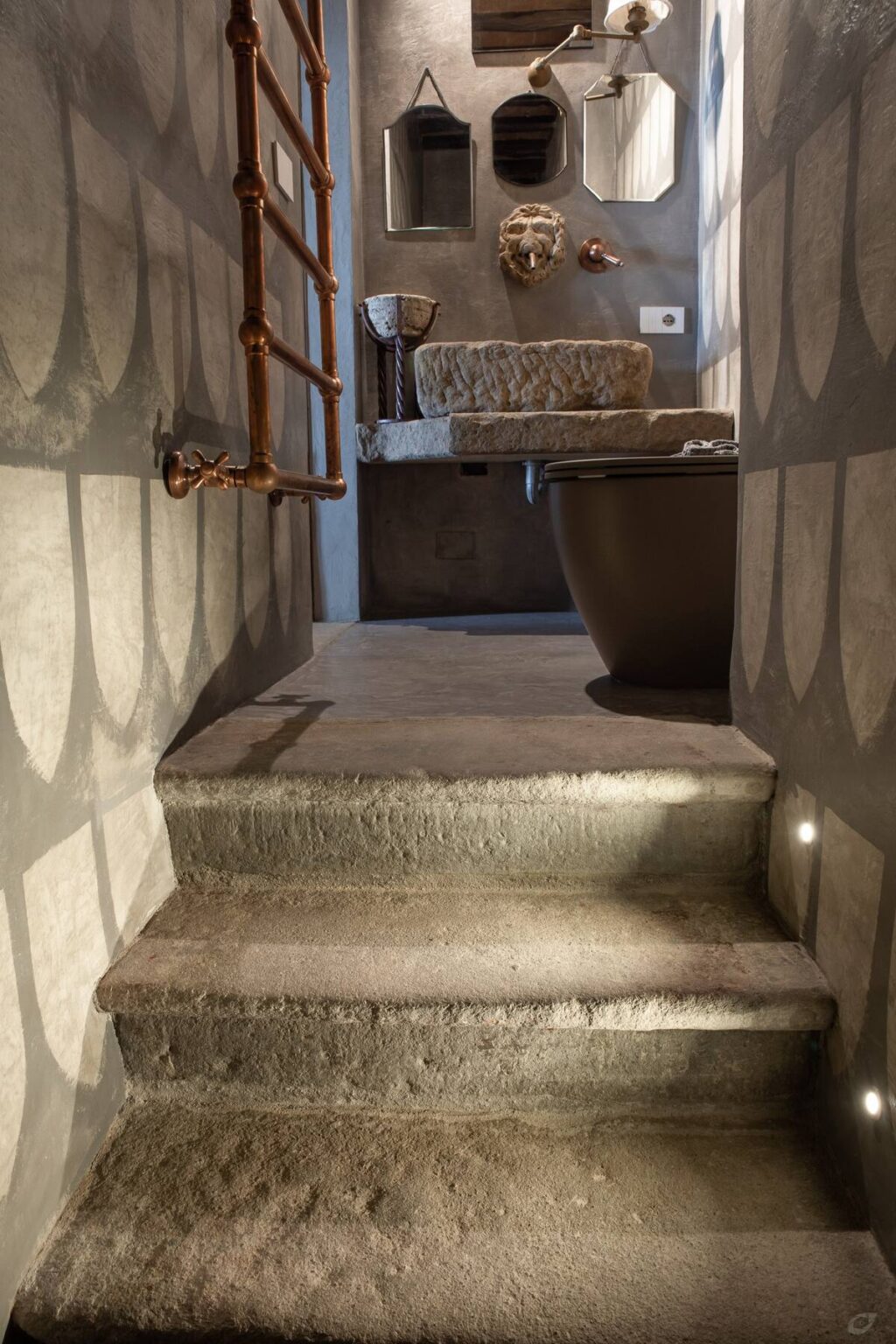 Interior view of a modern bathroom featuring a concrete step leading to a stylish toilet, with exposed plumbing and minimalist design elements. Soft lighting enhances the textures of the materials used. | Only on SopranoVillas