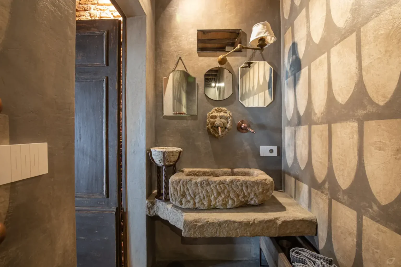 Modern bathroom design featuring a stone sink, textured wall, and decorative mirrors. The space combines rustic elements with contemporary aesthetics, showcasing a unique blend of materials and stylish decor. | Only on SopranoVillas