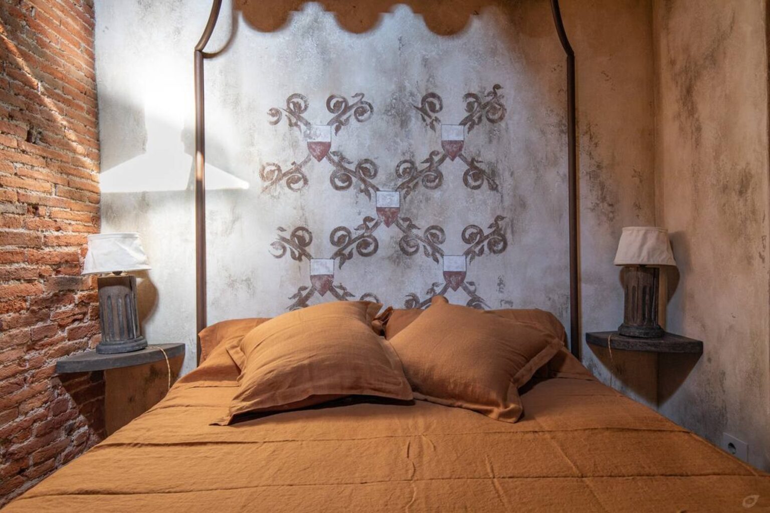 Cozy bedroom featuring a warm-toned bedspread and pillows, with decorative wall art and rustic brick accents, complemented by stylish bedside lamps. | Only on SopranoVillas
