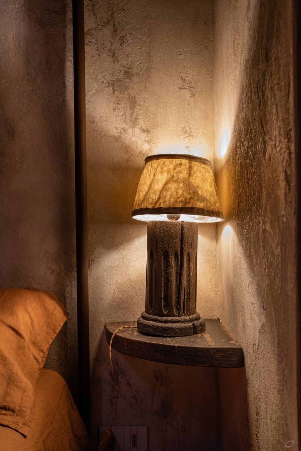 Table lamp with a beige shade, casting warm light against a textured wall, creating a cozy ambiance in a dimly lit room. | Only on SopranoVillas