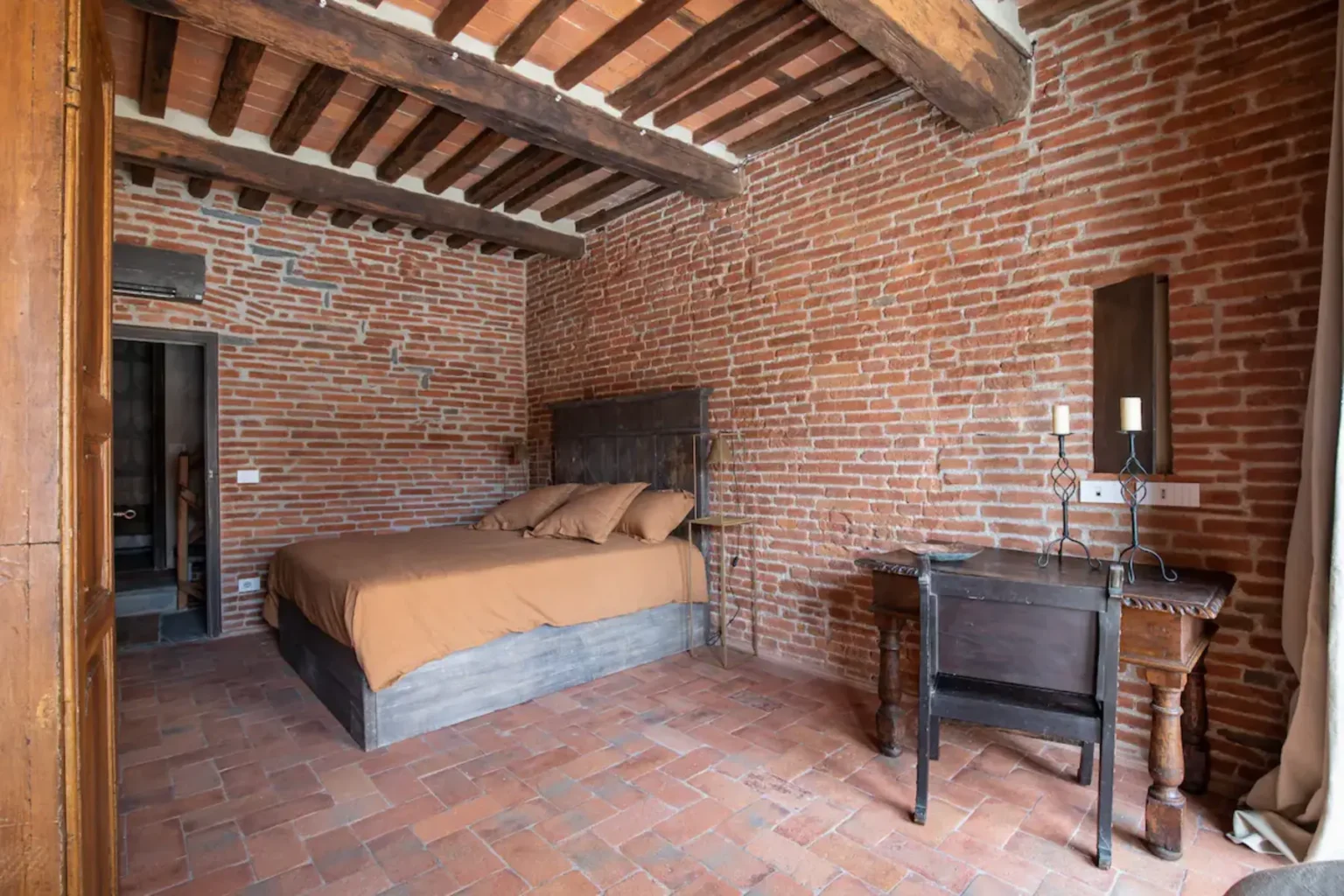 Cozy bedroom featuring exposed brick walls, wooden beams, a comfortable bed with brown bedding, and a vintage wooden dresser with a mirror, creating a rustic and inviting atmosphere. | Only on SopranoVillas