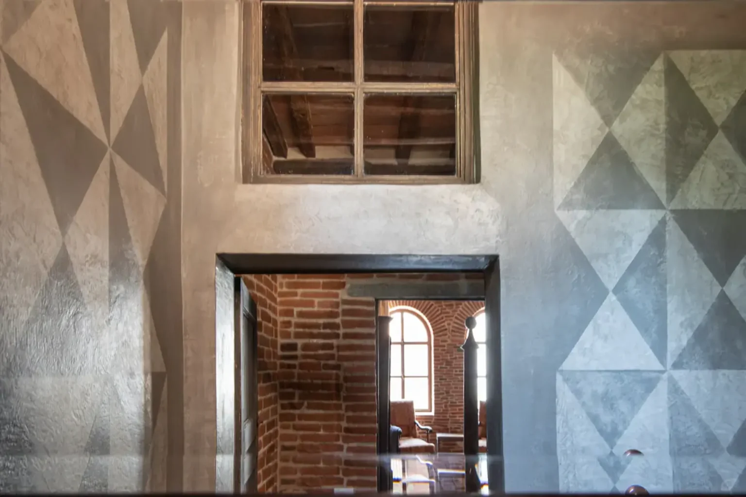 Interior view showcasing a modern architectural design with textured gray walls featuring geometric patterns, a brick archway, and a wooden window above. Natural light filters through the window, enhancing the contemporary aesthetic of the space. | Only on SopranoVillas