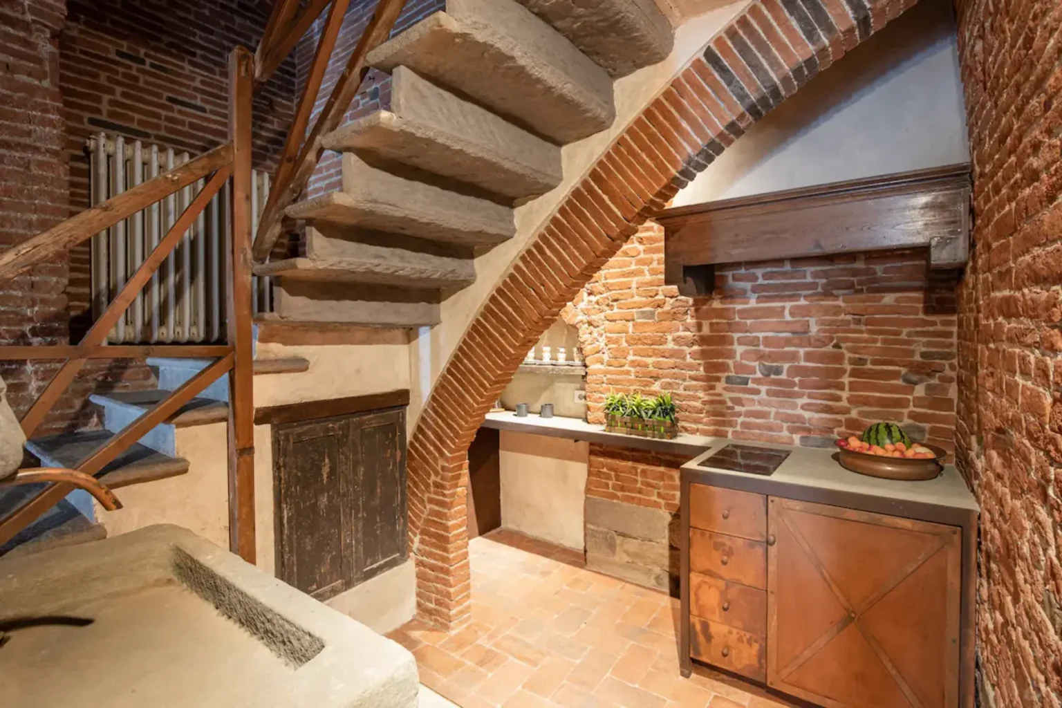 Cozy kitchen area featuring rustic brick walls, wooden cabinetry, and a unique curved staircase. The space combines traditional and modern design elements, creating an inviting atmosphere. | Only on SopranoVillas