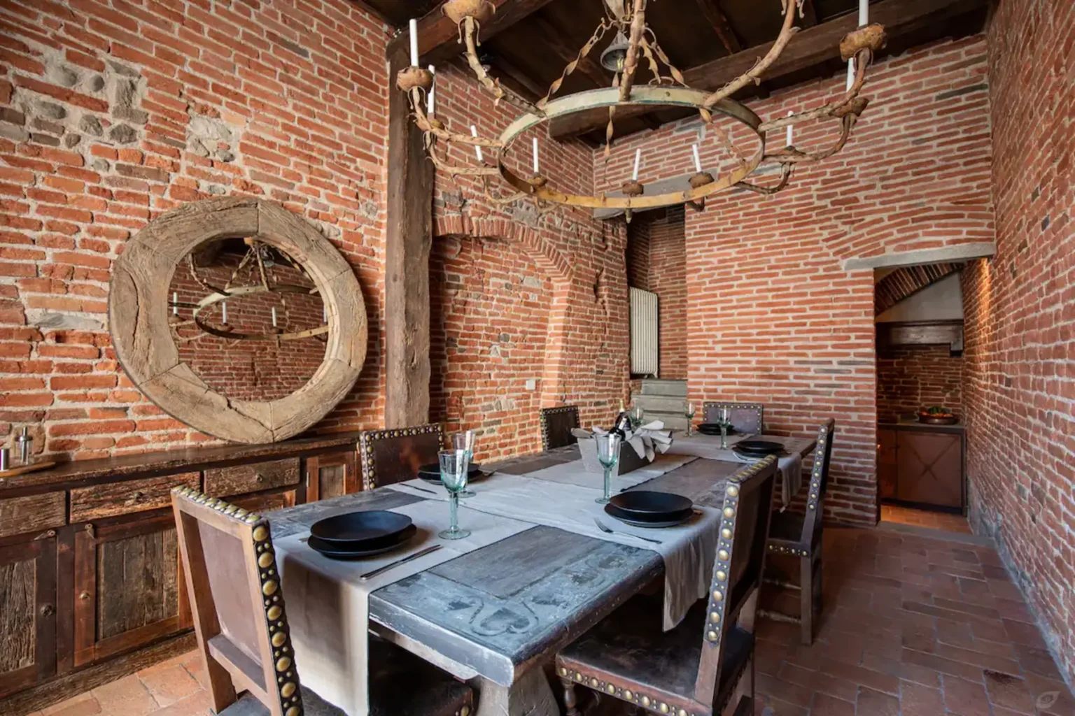Rustic dining room featuring exposed brick walls, a wooden dining table set for six, and a unique chandelier made from branches, creating a warm and inviting atmosphere. | Only on SopranoVillas
