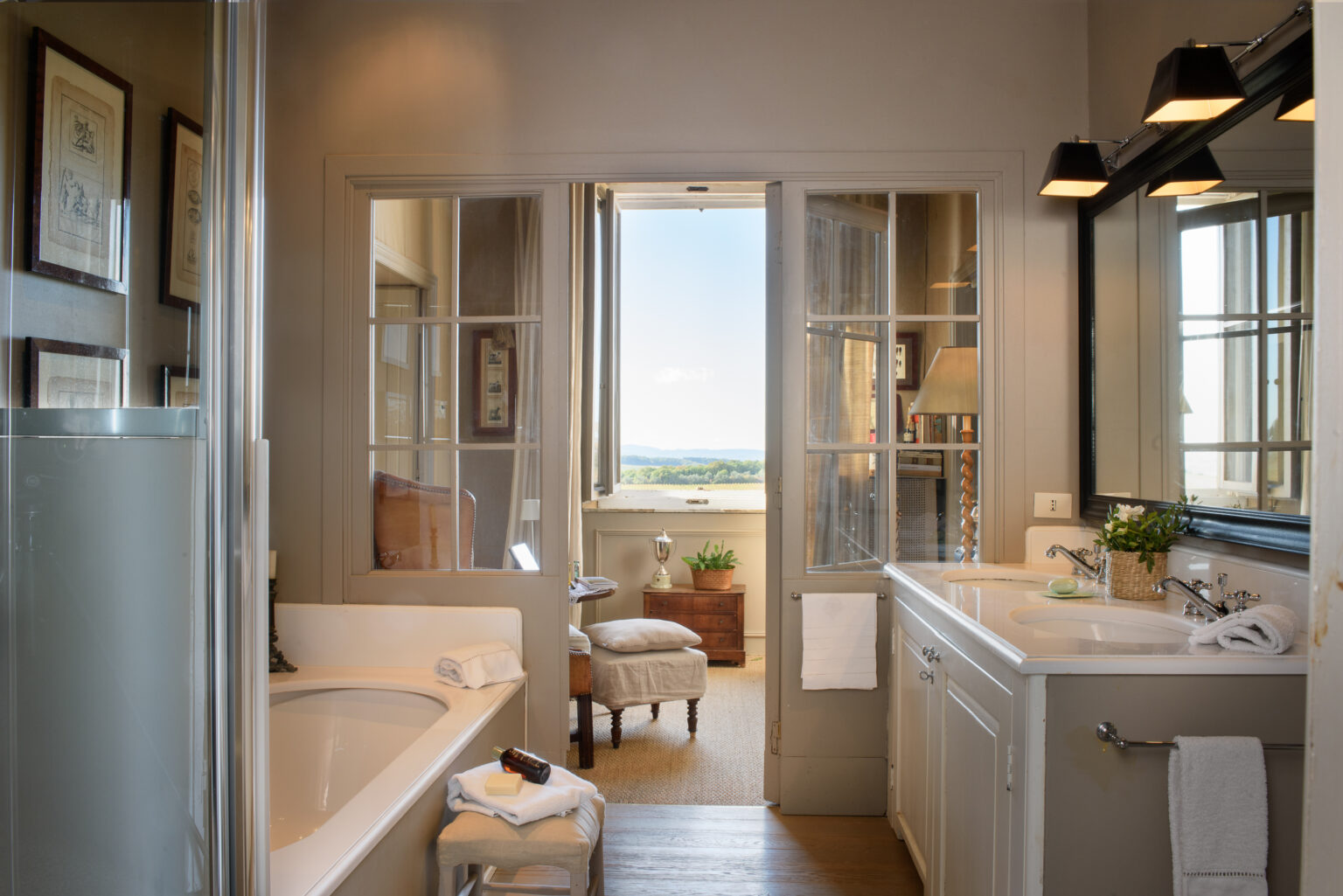 Elegant bathroom design featuring a modern bathtub, double vanity with sleek fixtures, and large windows offering scenic views. The space is adorned with framed art and natural light, creating a serene atmosphere. | Only on SopranoVillas