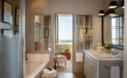 Elegant bathroom design featuring a modern bathtub, double vanity with sleek fixtures, and large windows offering scenic views. The space is adorned with framed art and natural light, creating a serene atmosphere.