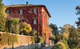 Historic red brick building surrounded by autumn foliage in a serene landscape.