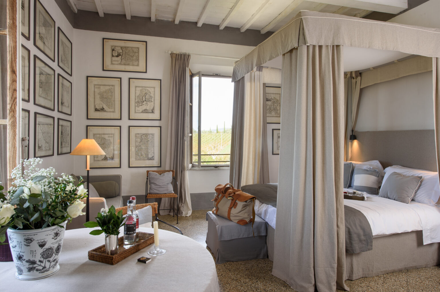 Elegant bedroom featuring a four-poster bed, framed artwork on the walls, and a cozy seating area. Natural light streams through the window, highlighting the tasteful decor and floral arrangements. Ideal for a relaxing retreat. | Only on SopranoVillas