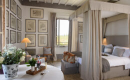 Elegant bedroom featuring a four-poster bed, framed artwork on the walls, and a cozy seating area. Natural light streams through the window, highlighting the tasteful decor and floral arrangements. Ideal for a relaxing retreat.