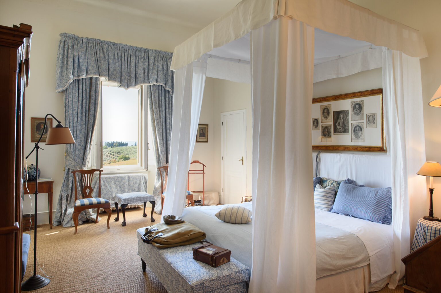 Elegant bedroom featuring a four-poster bed with sheer drapes, cozy blue and white decor, and a scenic view through large windows. The room includes vintage furniture, soft lighting, and a warm, inviting atmosphere perfect for relaxation. | Only on SopranoVillas