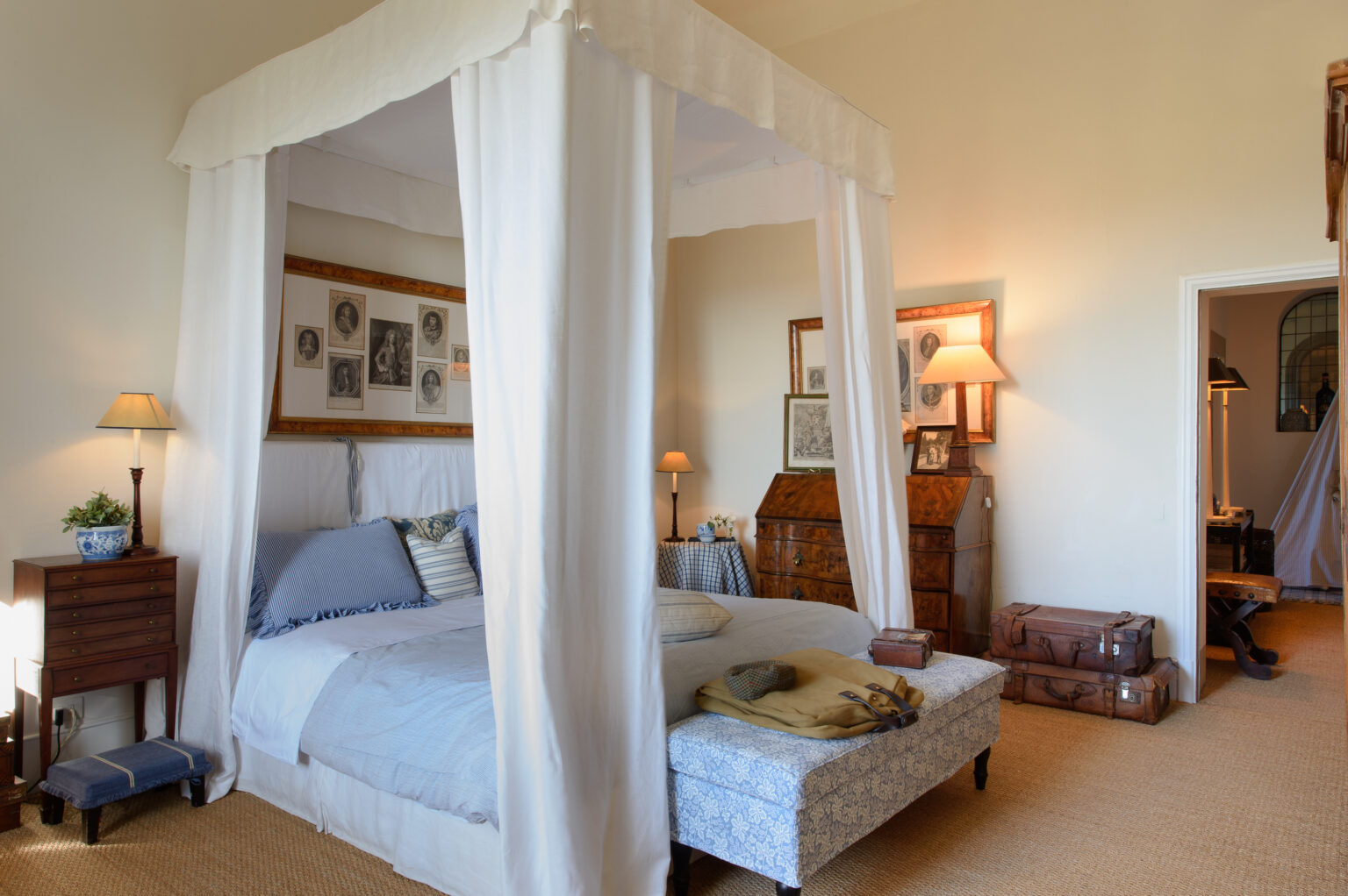 Spacious bedroom featuring a four-poster bed draped with white fabric, soft blue bedding, vintage decor, and warm lighting from bedside lamps, creating a cozy and inviting atmosphere. | Only on SopranoVillas