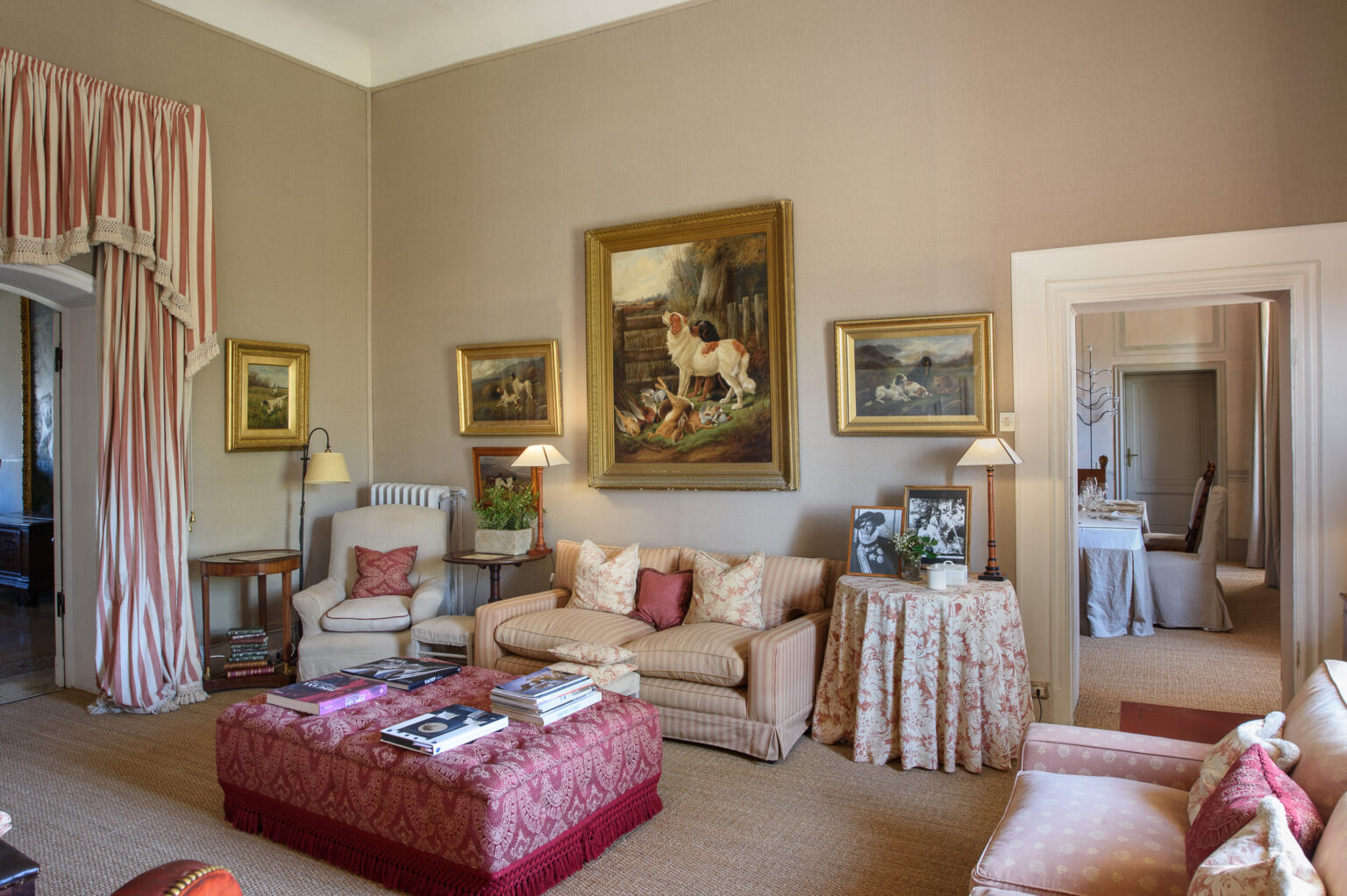 Elegant living room featuring plush seating, decorative pillows, and an ornate coffee table. The walls are adorned with classic paintings, and large windows are dressed with flowing drapes, creating a warm and inviting atmosphere. | Only on SopranoVillas