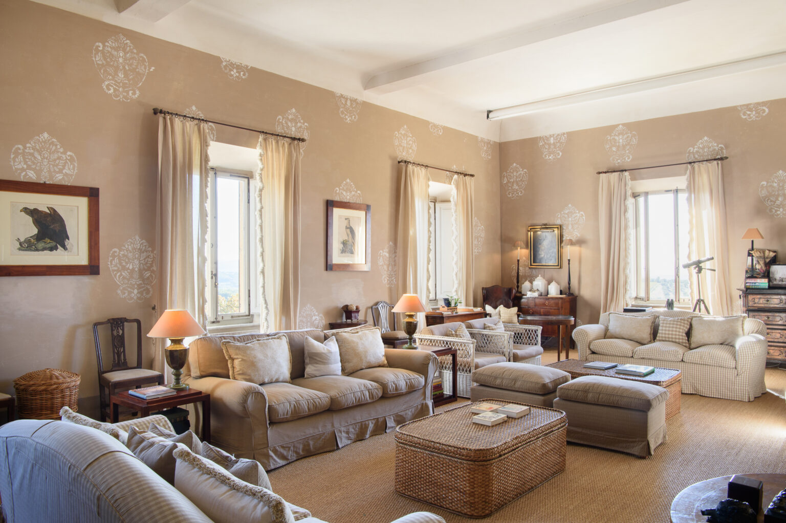 Spacious and elegantly designed living room featuring beige walls, large windows with soft drapes, comfortable seating, a wooden coffee table, and decorative accents, creating a warm and inviting atmosphere. | Only on SopranoVillas