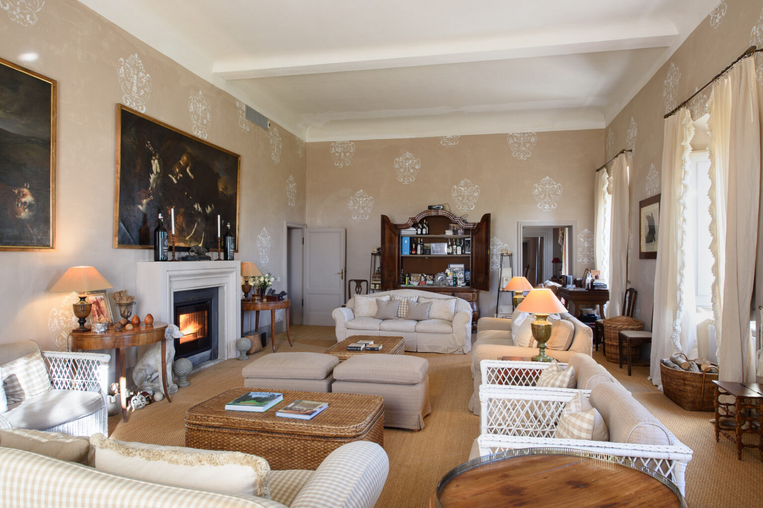 Elegant living room featuring plush sofas, a cozy fireplace, and vintage decor. The room is adorned with artwork and has large windows allowing natural light, creating a warm and inviting atmosphere. | Only on SopranoVillas