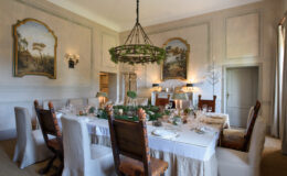 Elegant dining room featuring a large table set for a formal meal, adorned with greenery and decorative tableware. The room showcases classic wall art, a chandelier, and stylish seating, creating a sophisticated atmosphere for gatherings.