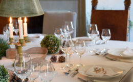 Elegant dining table set for a festive meal, featuring candles, wine glasses, and decorative elements like pinecones and greenery, creating a warm and inviting atmosphere.