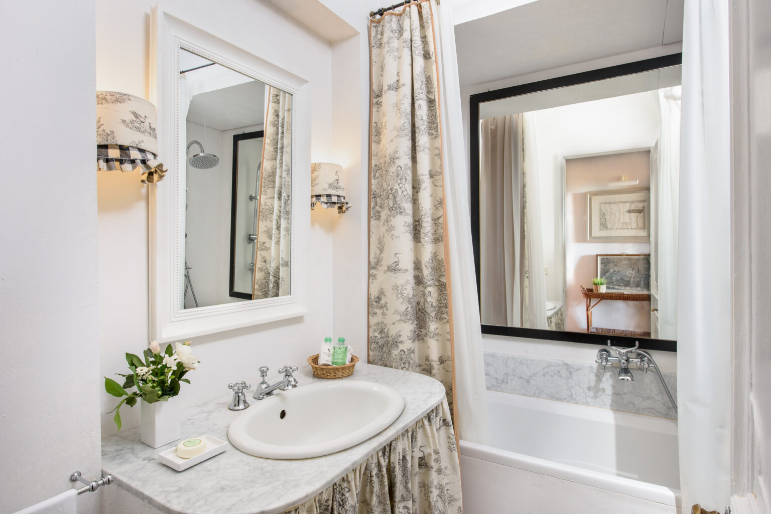Elegant bathroom featuring a marble countertop sink, decorative wall mirror, and a bathtub with a glass enclosure. Soft, neutral tones and floral curtains enhance the inviting atmosphere. | Only on SopranoVillas