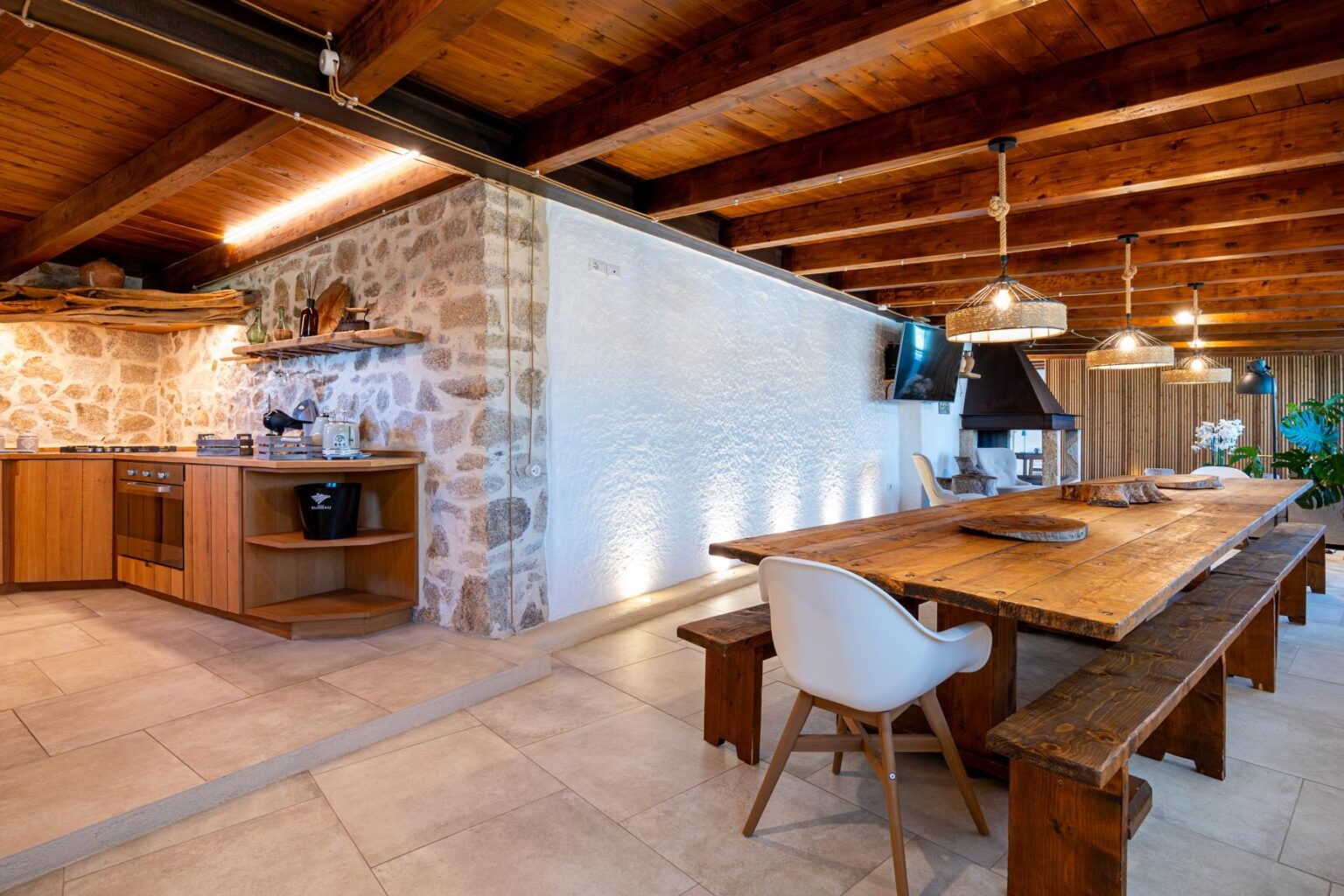 Modern kitchen and dining area featuring wooden beams, stone walls, a large wooden table, and contemporary furnishings, creating a warm and inviting atmosphere. | Only on SopranoVillas