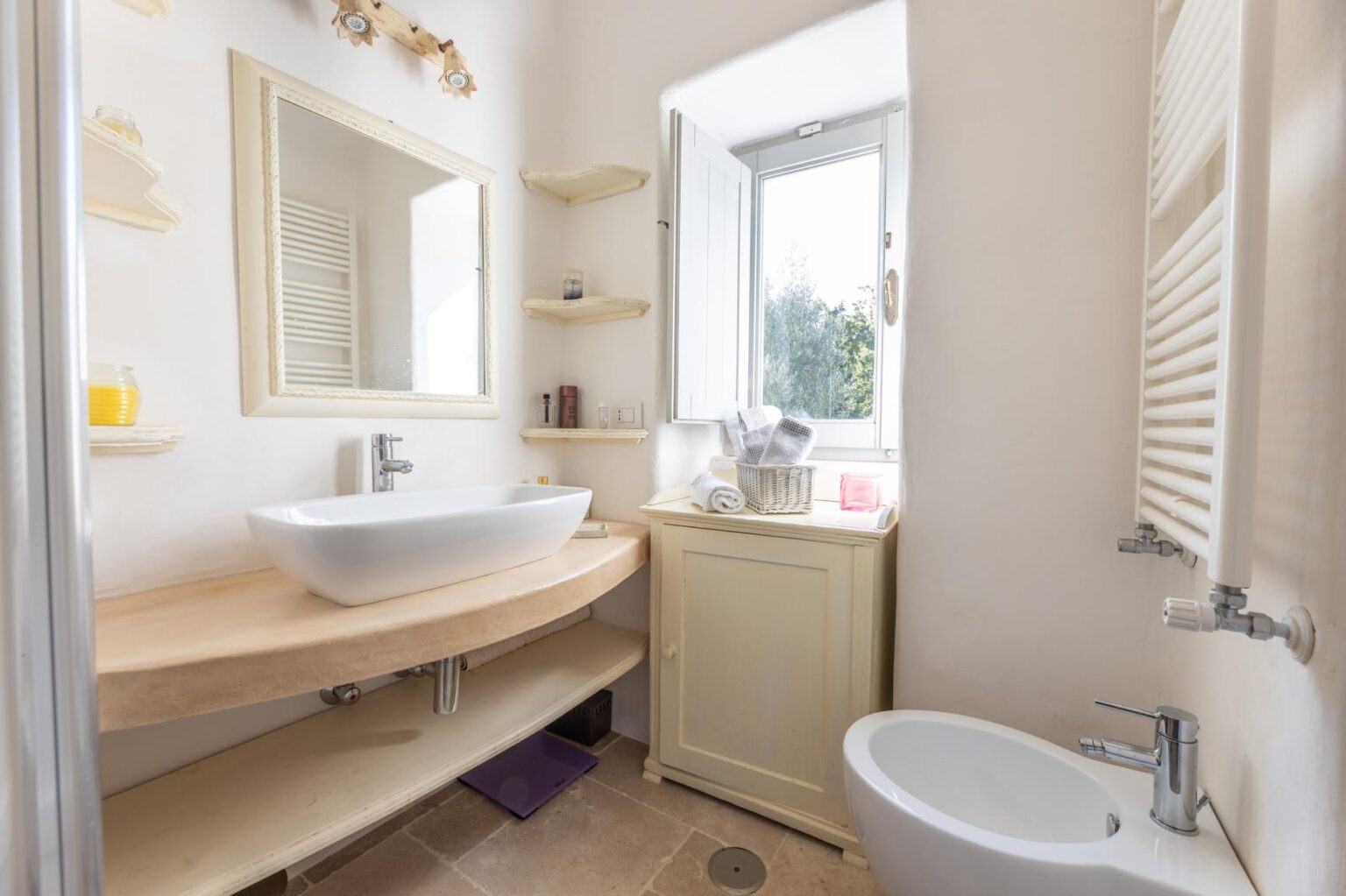 Modern bathroom interior featuring a stylish vessel sink on a wooden countertop, natural light from a window, a bidet, and elegant shelving for storage. | Only on SopranoVillas