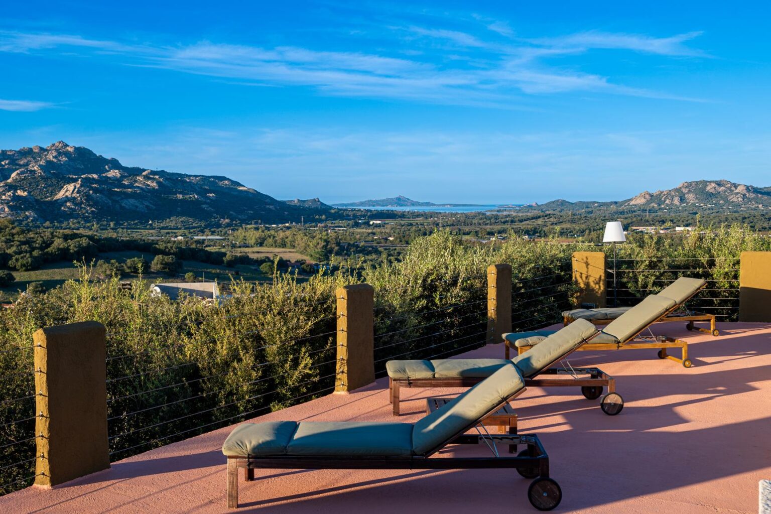 Scenic view from a terrace with two lounge chairs overlooking lush greenery and distant mountains under a clear blue sky. Perfect for relaxation and enjoying nature. | Only on SopranoVillas