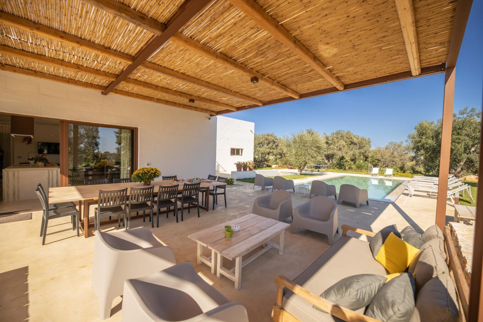 Modern outdoor patio with comfortable seating, dining area, and swimming pool in a sunny landscape. Ideal for relaxation and entertaining guests. | Only on SopranoVillas