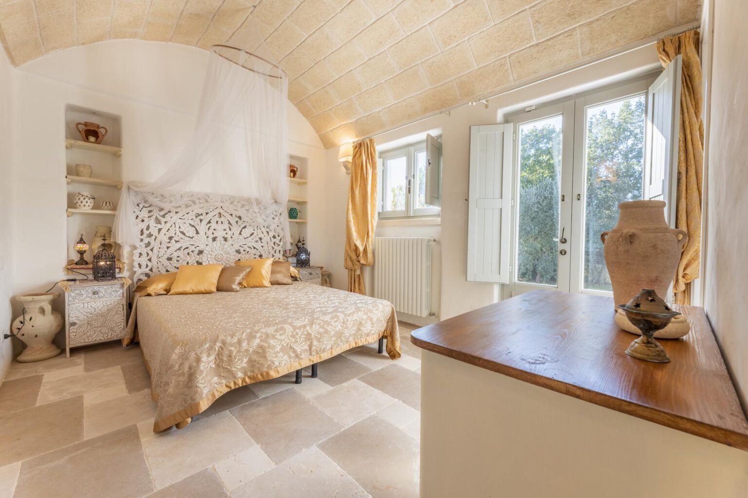 Cozy bedroom with a decorative bedspread, yellow accent pillows, and large windows allowing natural light, featuring wooden furniture and a soft color palette for a warm atmosphere. | Only on SopranoVillas
