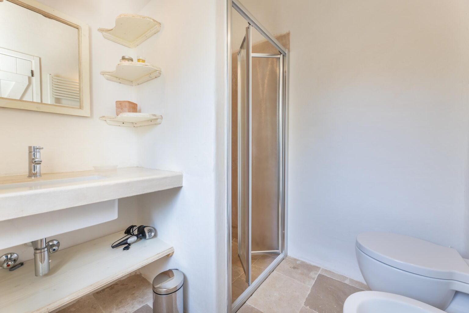 Modern bathroom featuring a glass shower, sleek countertop with sink, wall-mounted shelves, and a toilet. The neutral color palette creates a clean and spacious atmosphere. | Only on SopranoVillas