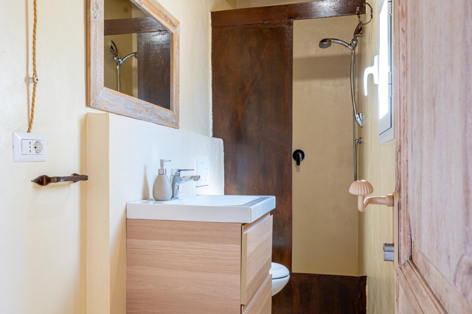 Modern bathroom interior featuring a wooden vanity with a sink, a mirror, and a shower area, complemented by warm yellow walls and rustic wooden accents. | Only on SopranoVillas