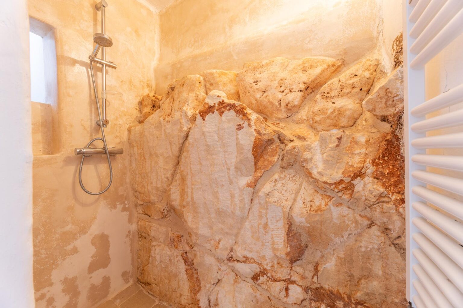 Modern shower design featuring a natural stone wall, showcasing warm beige tones and a sleek shower fixture. The minimalist space emphasizes a blend of luxury and natural elements, ideal for contemporary bathroom aesthetics. | Only on SopranoVillas