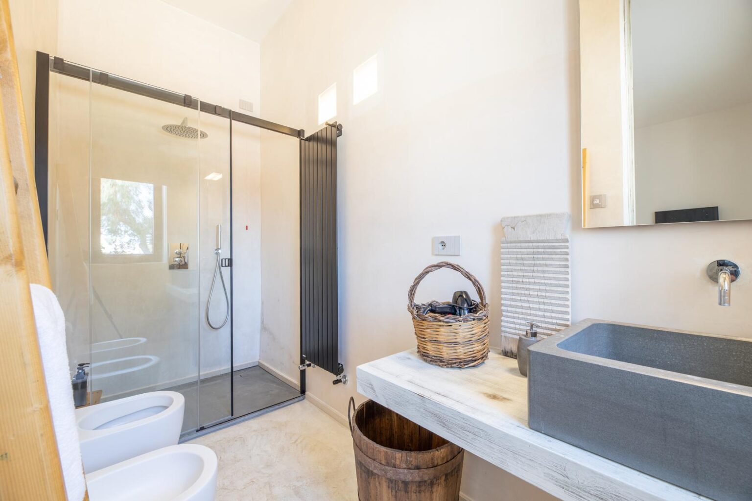 Modern bathroom featuring a glass shower enclosure, stylish sink with a concrete basin, and wooden accents. The space is well-lit with natural light, showcasing a clean and minimalist design. | Only on SopranoVillas