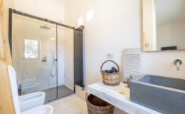 Modern bathroom featuring a glass shower enclosure, stylish sink with a concrete basin, and wooden accents. The space is well-lit with natural light, showcasing a clean and minimalist design.