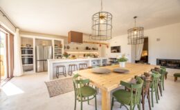 Bright and airy modern kitchen with a spacious dining area featuring a large wooden table surrounded by green chairs, pendant lighting, and open shelving, creating a welcoming atmosphere for family gatherings.