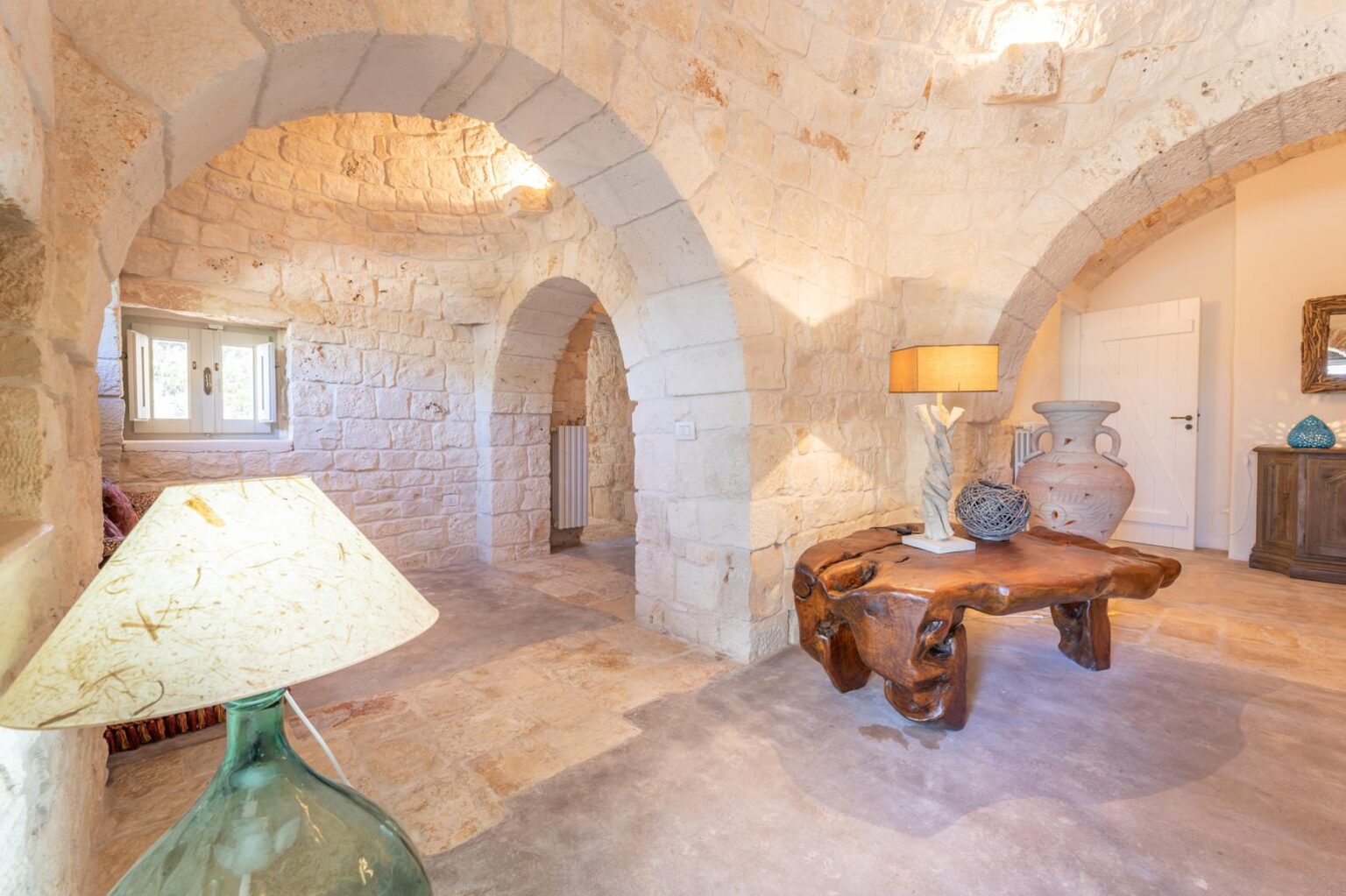 Interior view of a rustic stone house featuring arched ceilings, a wooden coffee table, a decorative lamp, and traditional pottery, highlighting a cozy and inviting atmosphere. | Only on SopranoVillas