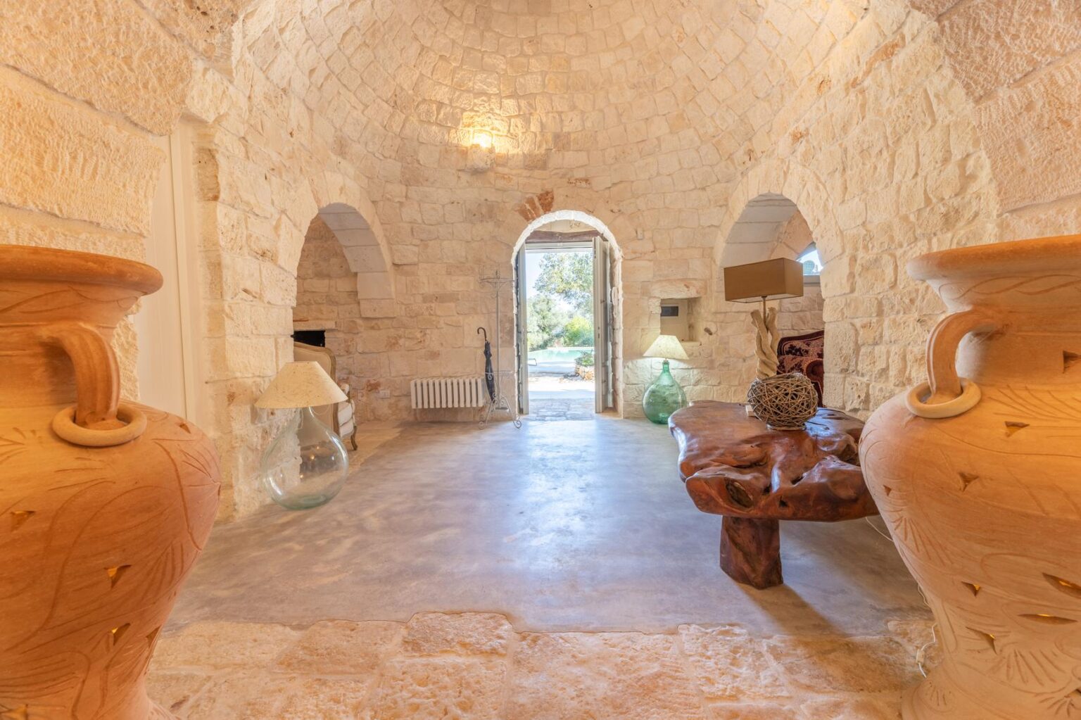 Interior view of a rustic stone hallway featuring large decorative pottery, arched doorways, and natural light illuminating the space, creating a warm and inviting atmosphere. | Only on SopranoVillas